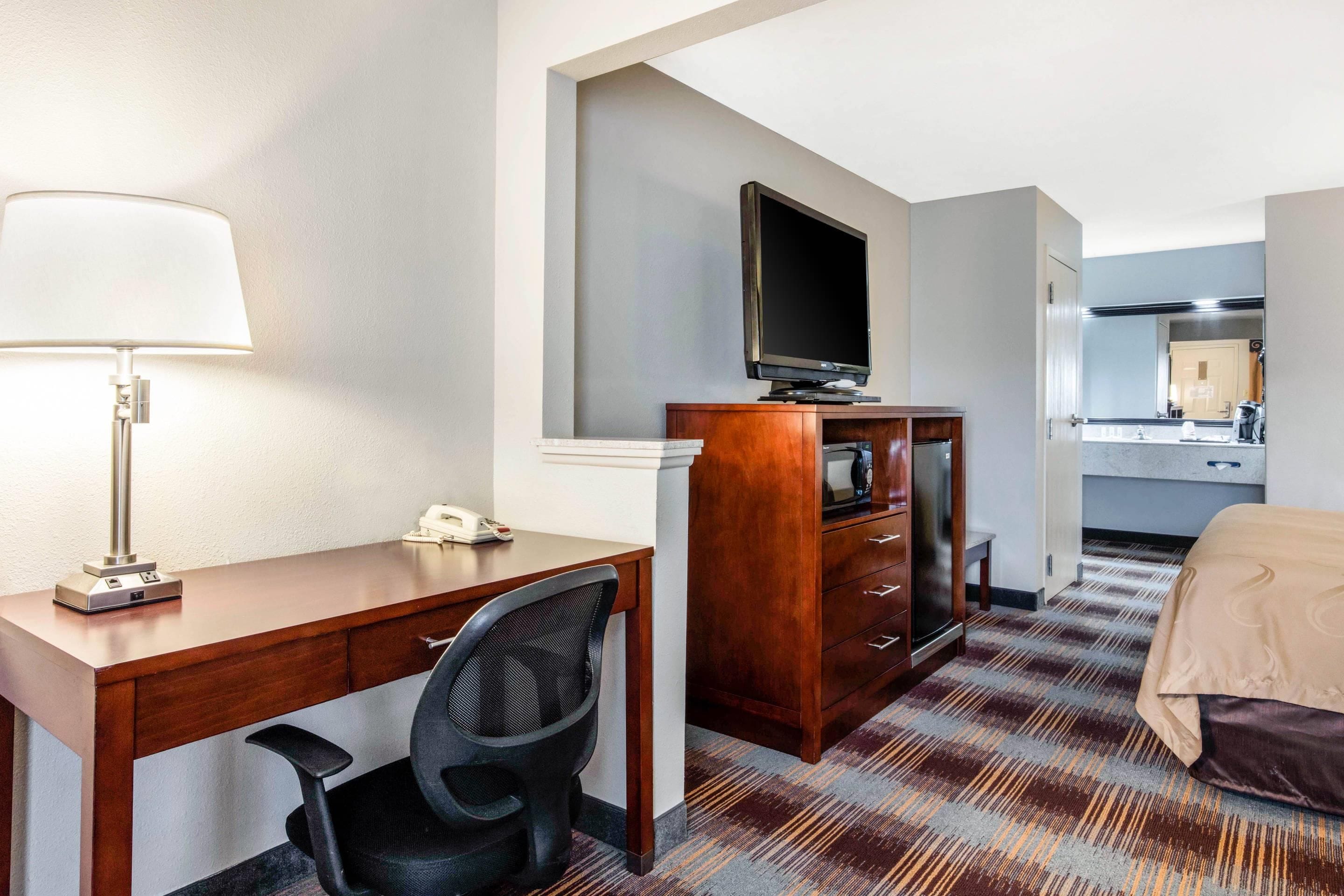 A hotel room with a desk, chair, television, and a bed.