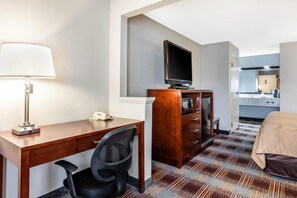 Quarto de hotel com escrivaninha, cadeira, televisão e cama.