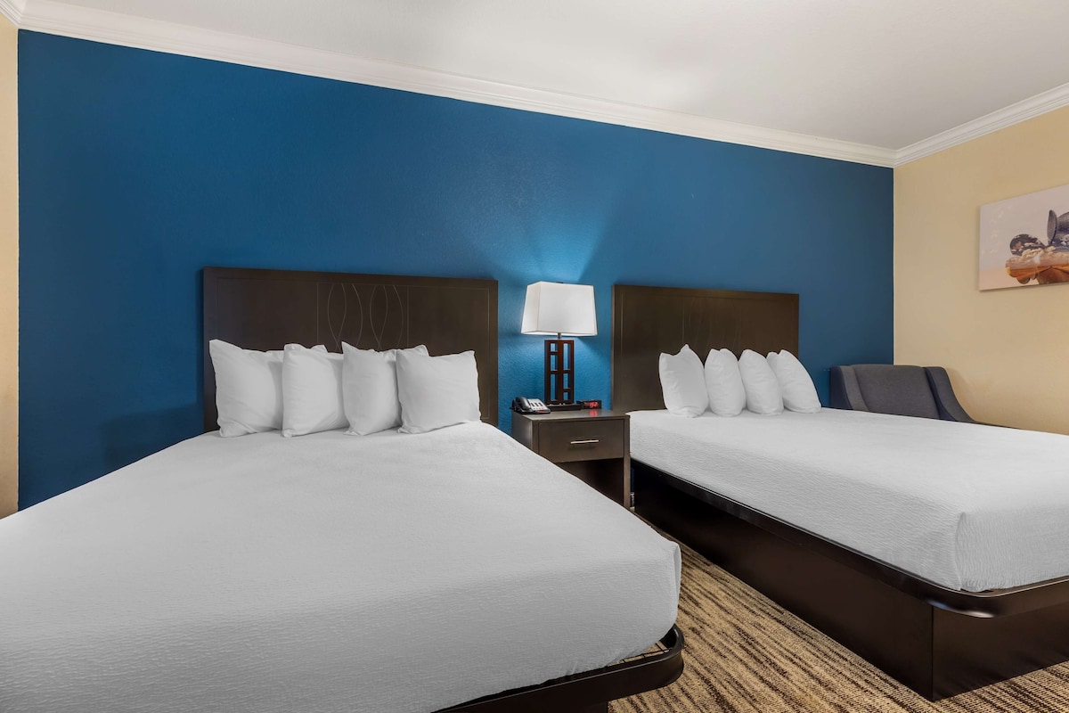 A hotel room with two beds, a nightstand with a lamp, and a painting on the wall.