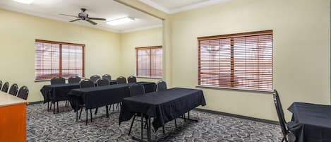 A conference room with a ceiling fan, large windows with blinds, and a carpeted floor.