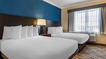 Habitación de hotel con dos camas, una mesita de noche con lámpara, una ventana con cortinas y vistas a la ciudad.