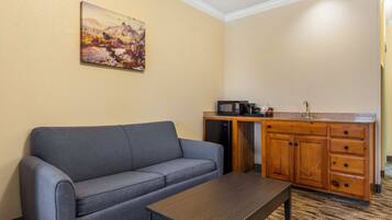 A room with a grey sofa, a wooden cabinet with a microwave, and a painting on the wall.