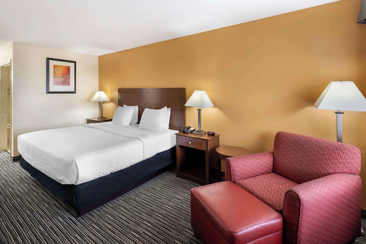 A hotel room with a large bed, two bedside tables with lamps, a red armchair, and a small table with a telephone.