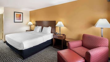 A hotel room with a large bed, two bedside tables with lamps, a red armchair, and a small table with a telephone.