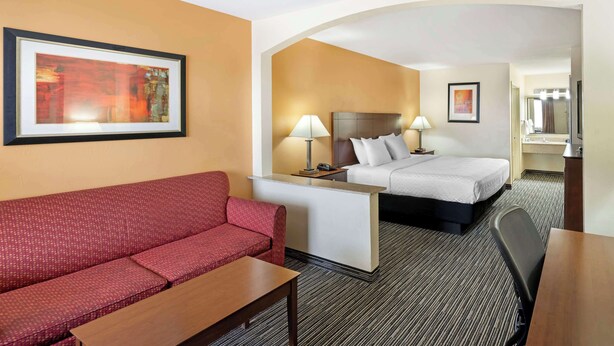 Une chambre d’hôtel avec un canapé rouge, un lit avec une literie blanche, un bureau avec une lampe et un tableau encadré au mur.
