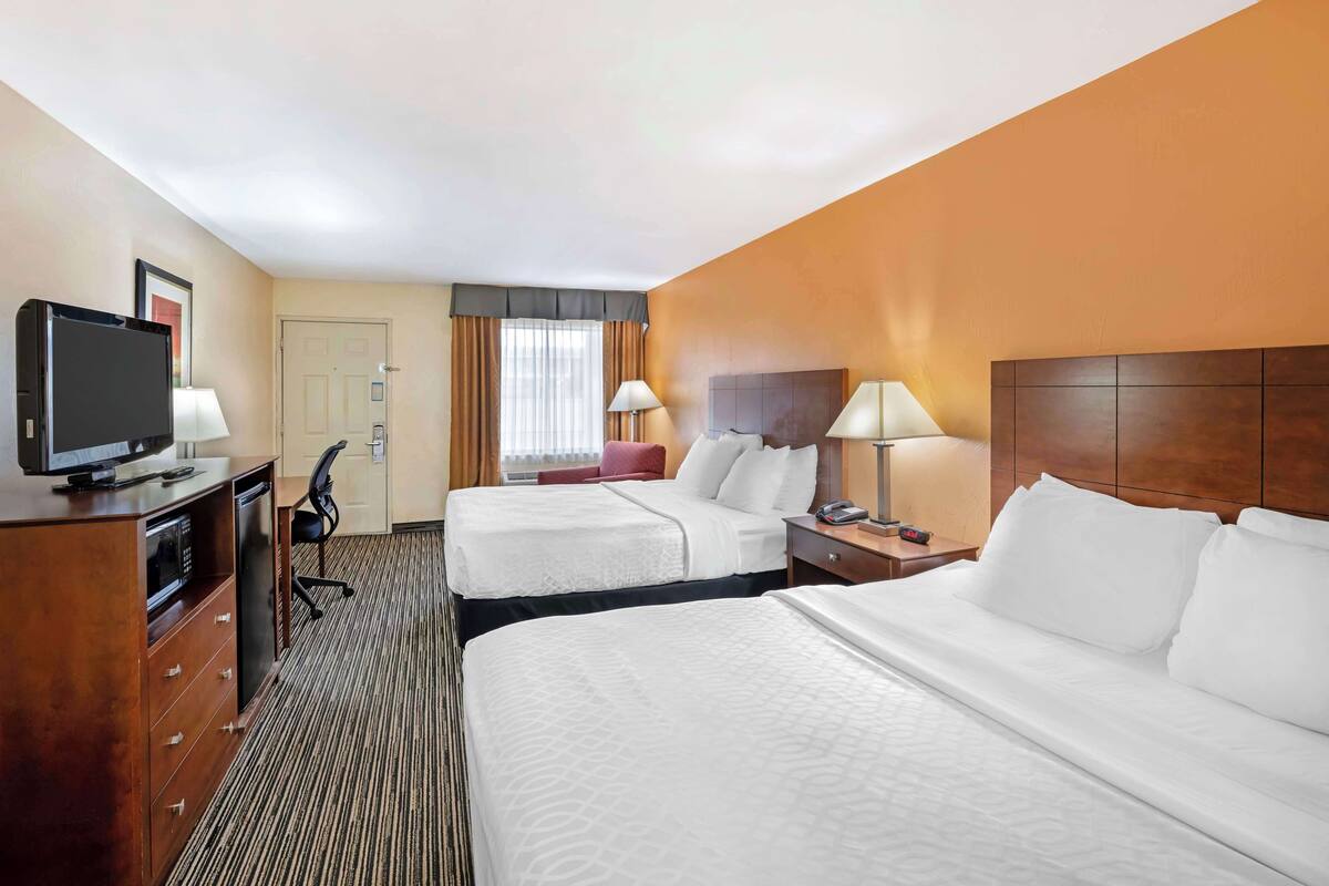 A hotel room with two beds, a TV, a desk, and a chair.