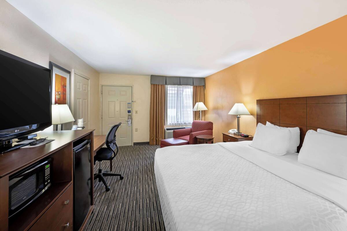 A hotel room with a large bed, a desk with a television, a chair, and two lamps.