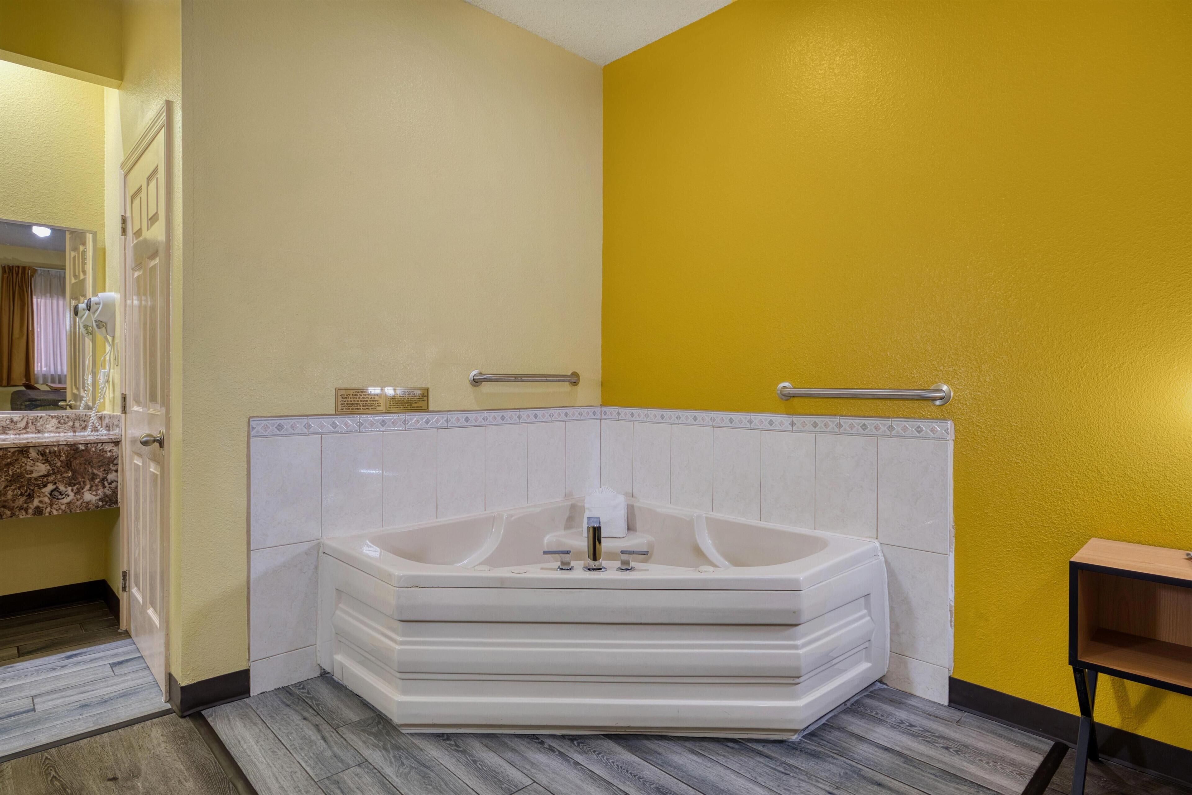 A bathroom with a large bathtub, a mirror, and a wooden bench.