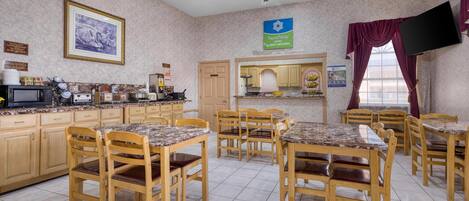Une chambre d’hôtel équipée d’un coin cuisine, d’une table à manger, de chaises, d’un ventilateur de plafond et d’un téléviseur fixé au mur.