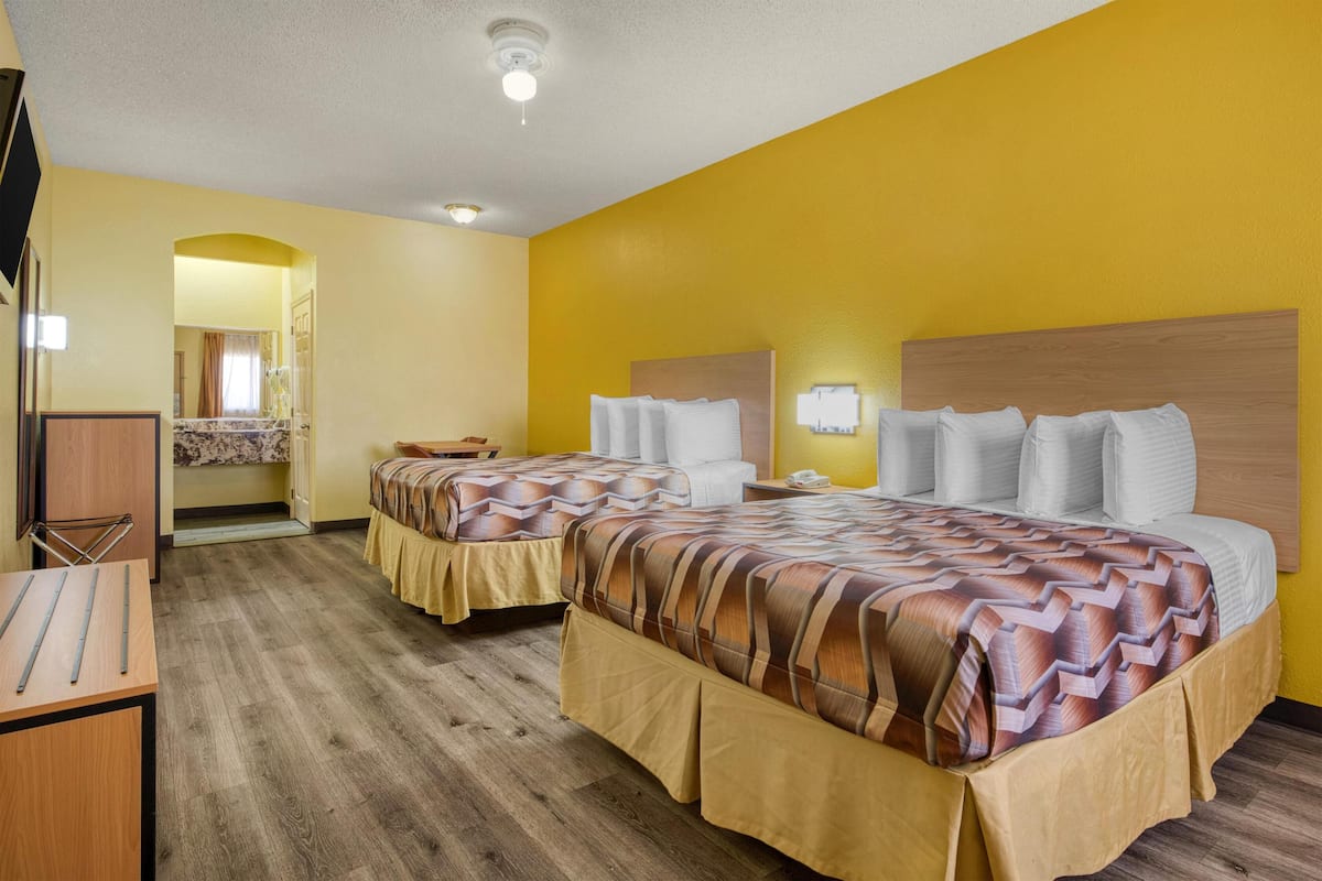 A hotel room with two beds, wooden flooring, a desk, and a bathroom visible through an archway.