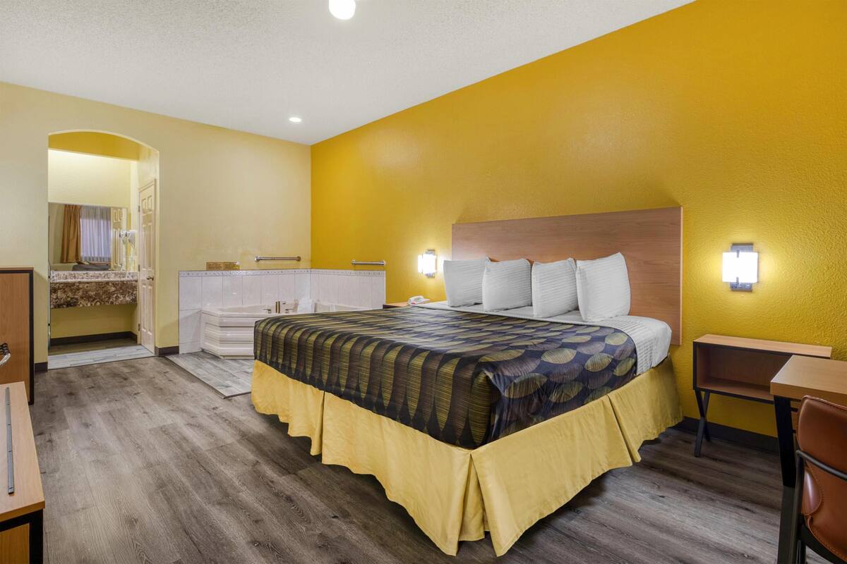 A hotel room with a bed, bedside table, lamp, and a view of the bathroom.