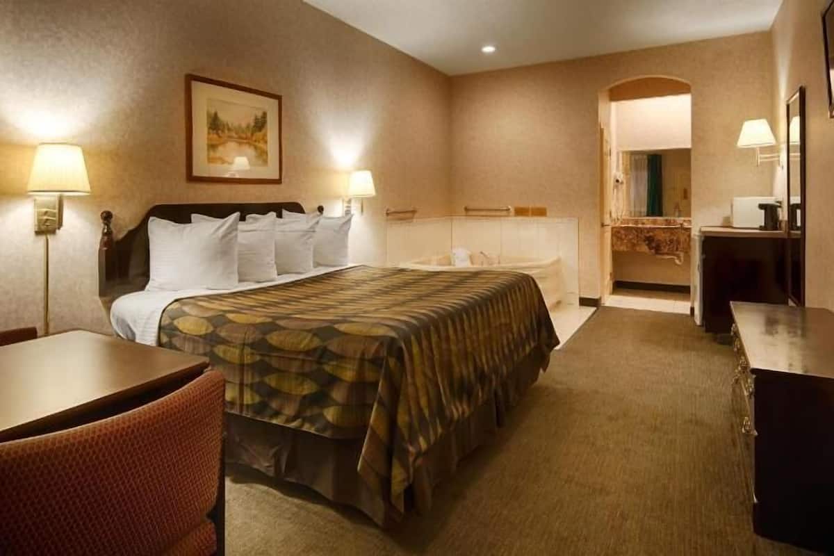 A hotel room with a bed, a desk, a chair, a bathroom, and a TV.