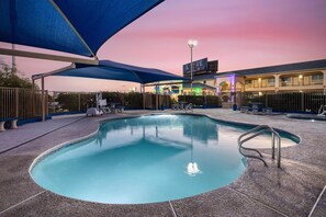 Una piscina con zona cubierta, cerca y un edificio con un cartel al fondo.