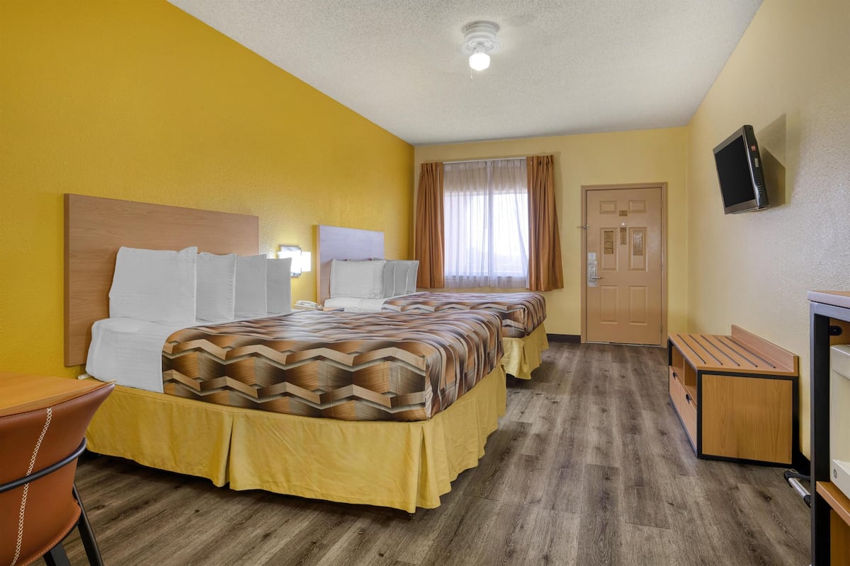 A hotel room with two beds, a desk, a chair, a television, and a door.