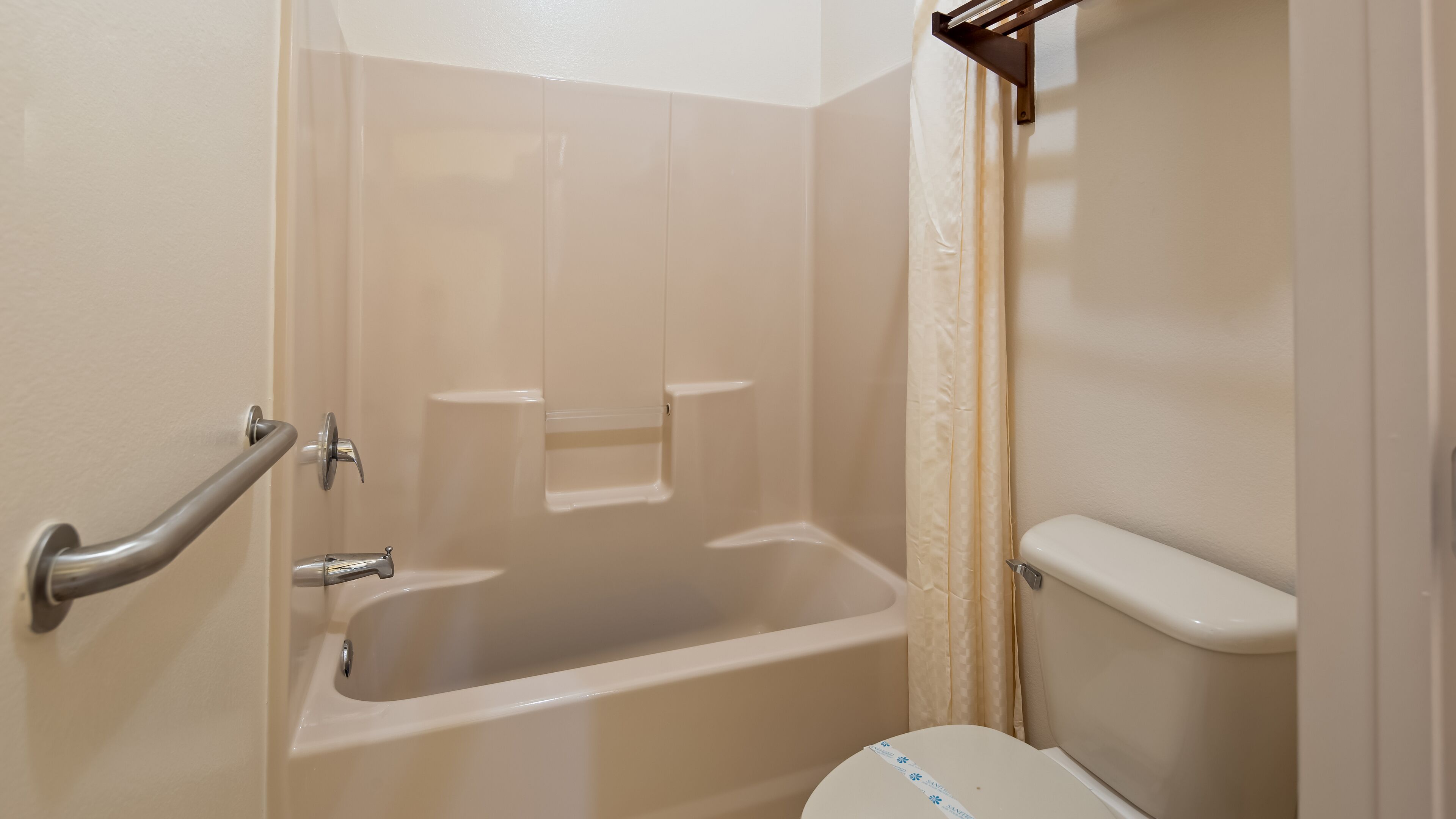 A bathroom with a bathtub, toilet, and grab bars.