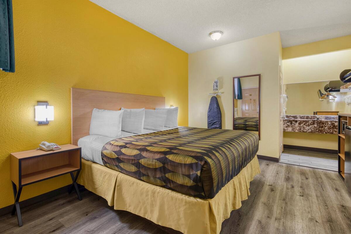 A hotel room with a bed, bedside table, lamp, and a small desk with a mirror.