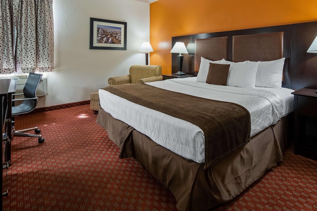 Une chambre d’hôtel avec un grand lit, deux lampes de chevet, un bureau avec une chaise et une fenêtre avec des rideaux.