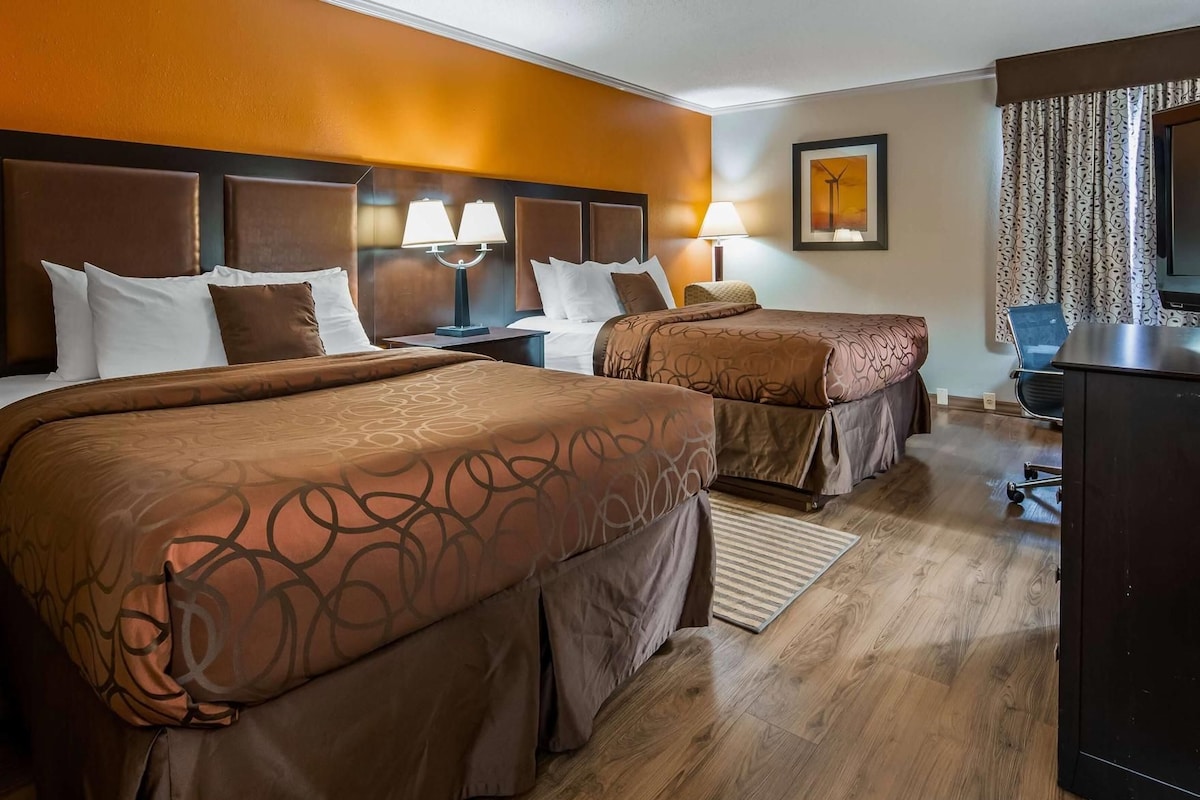 A hotel room with two beds, a desk, a chair, and a television.