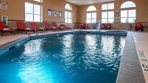 An indoor swimming pool with red lounge chairs and a tiled deck. - Baymont by Wyndham Lubbock (Lubbock)
