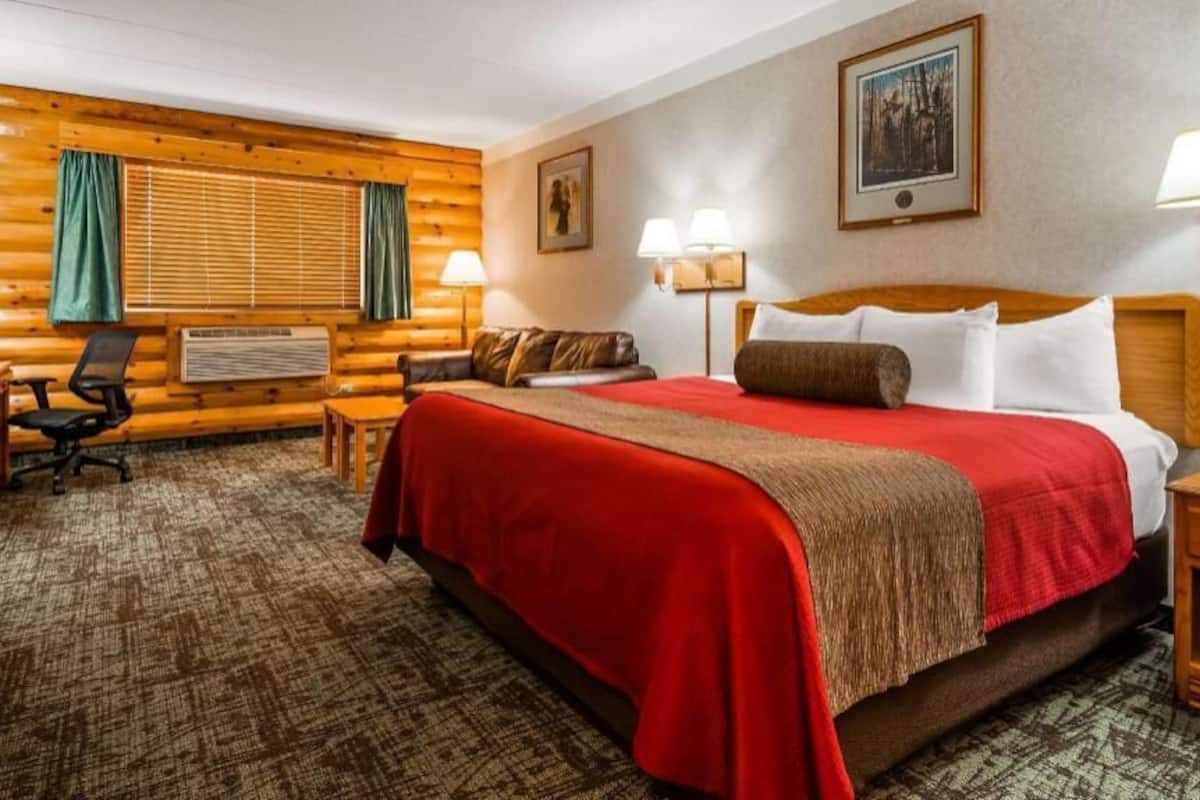 A hotel room with a large bed, a desk, a chair, a TV, and a fireplace.
