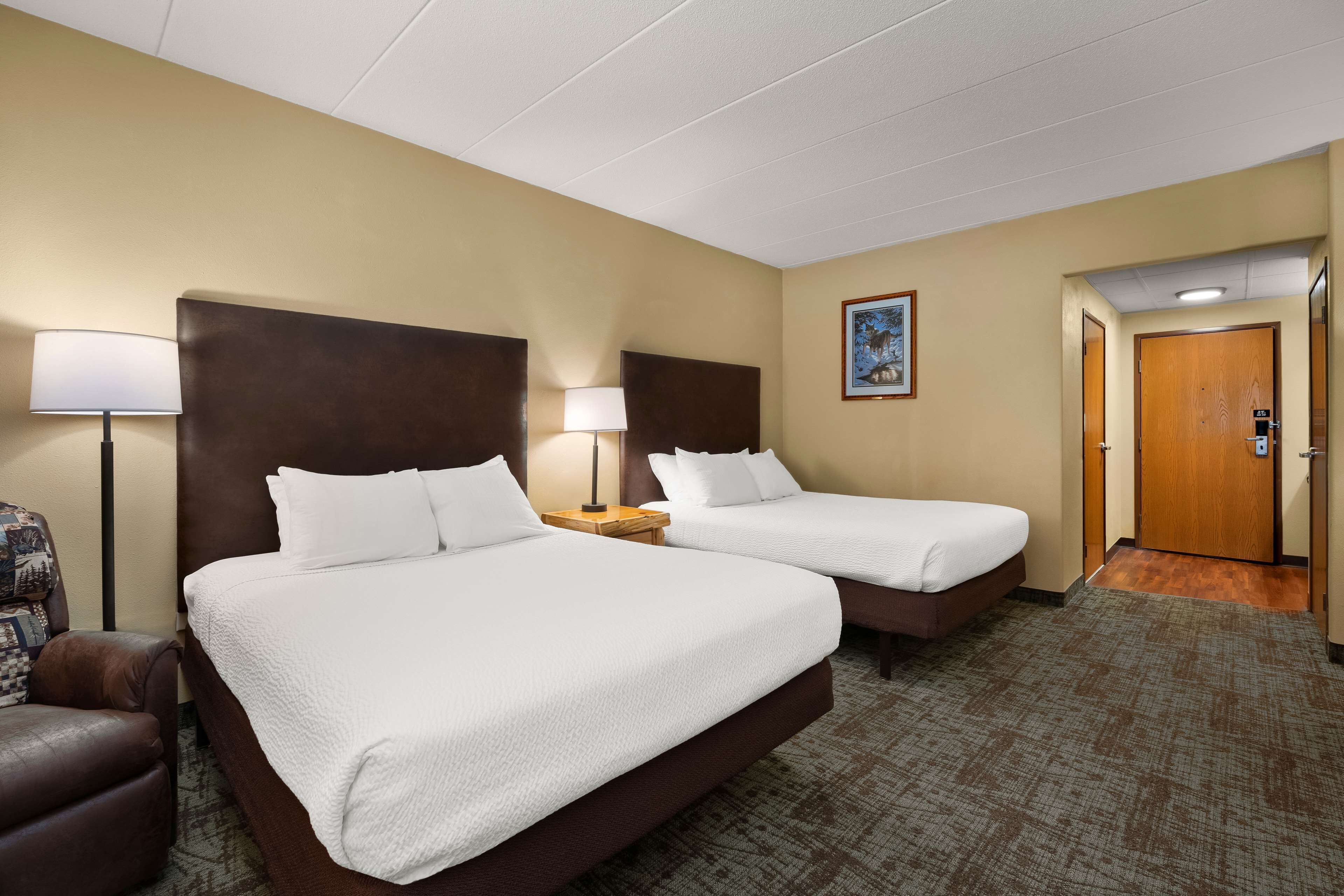 A hotel room with two beds, a desk, a chair, and a door.