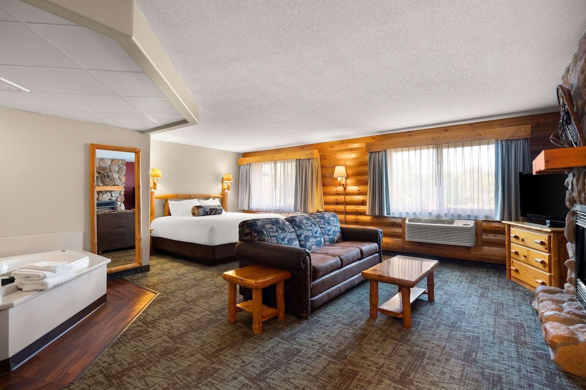 A hotel room with a bed, a sofa, a coffee table, a TV, and a bathroom with a sink and mirror.