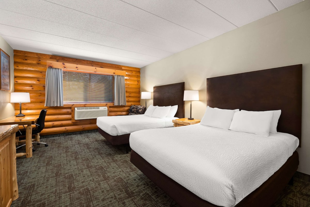 A hotel room with two beds, a desk, a chair, and a window with blinds.