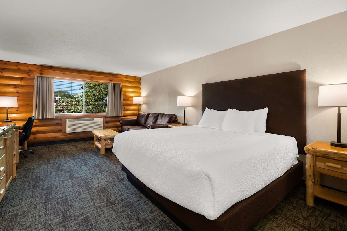 A hotel room with a large bed, a wooden desk, a chair, a small table, and a window with curtains.