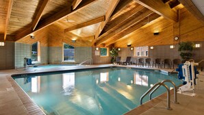 An indoor swimming pool with wooden beams on the ceiling, a lifeguard chair, and a seating area with chairs.