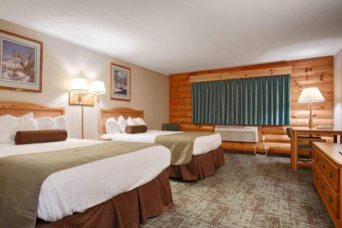 A hotel room with two beds, a desk, a chair, and a window with curtains.