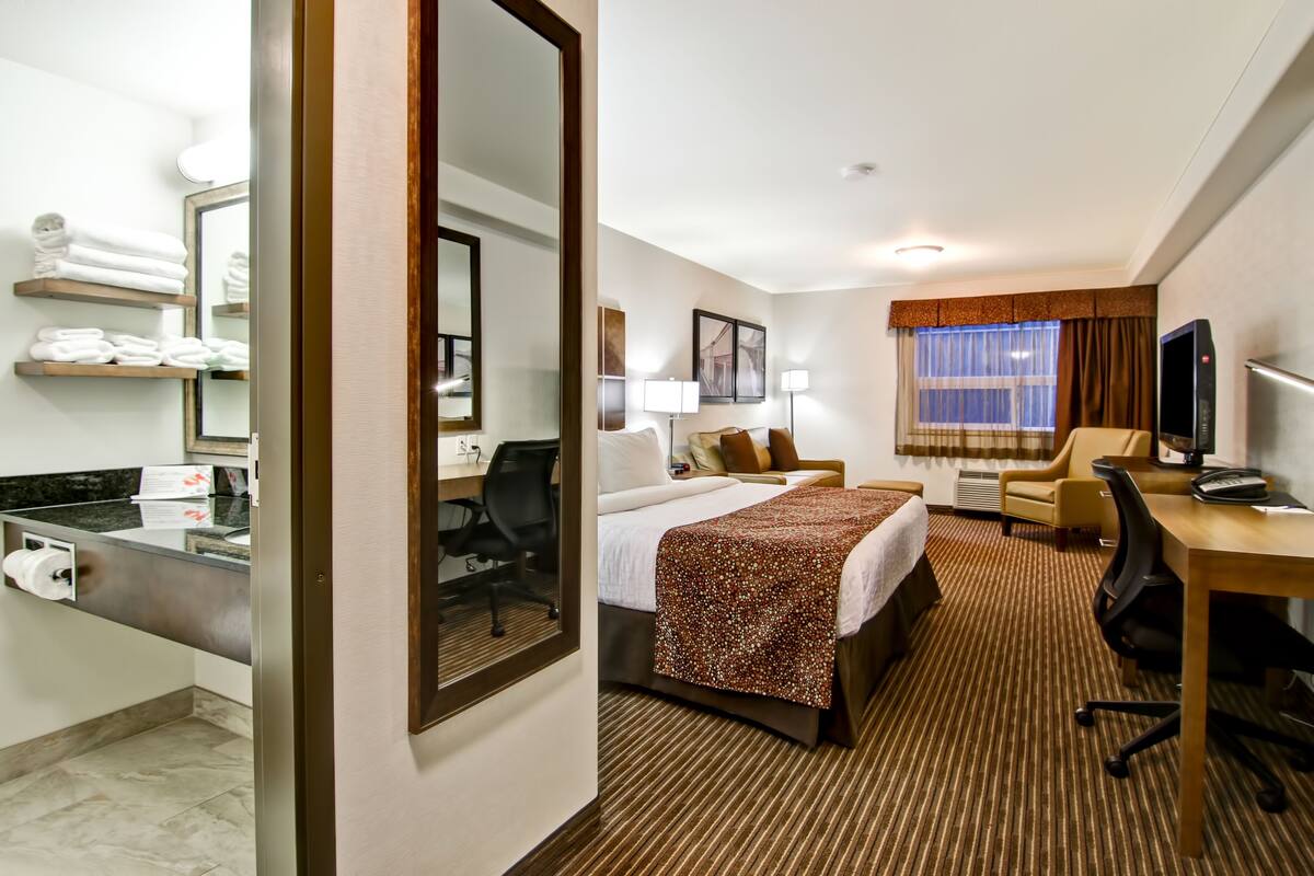 A hotel room with a bed, desk, chair, TV, and bathroom amenities.