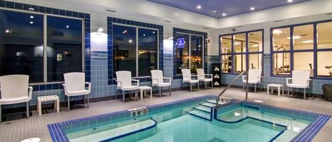 A swimming pool with chairs and a small table, surrounded by large windows.