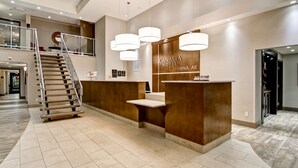 A hotel reception area with a modern design, including a reception desk, a staircase, and a sign for the CANALITA HOTEL in HANNNA, AB. - Canalta Hotel Hanna (Hanna)