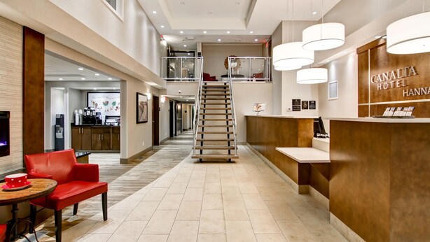 A hotel lobby with a reception desk, a staircase, and a seating area with a red chair and table. - Canalta Hotel Hanna (Hanna)