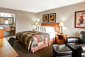 A hotel room with a bed, a desk, a chair, a lamp, and artwork on the walls. - Canalta Hotel Stettler (Stettler)