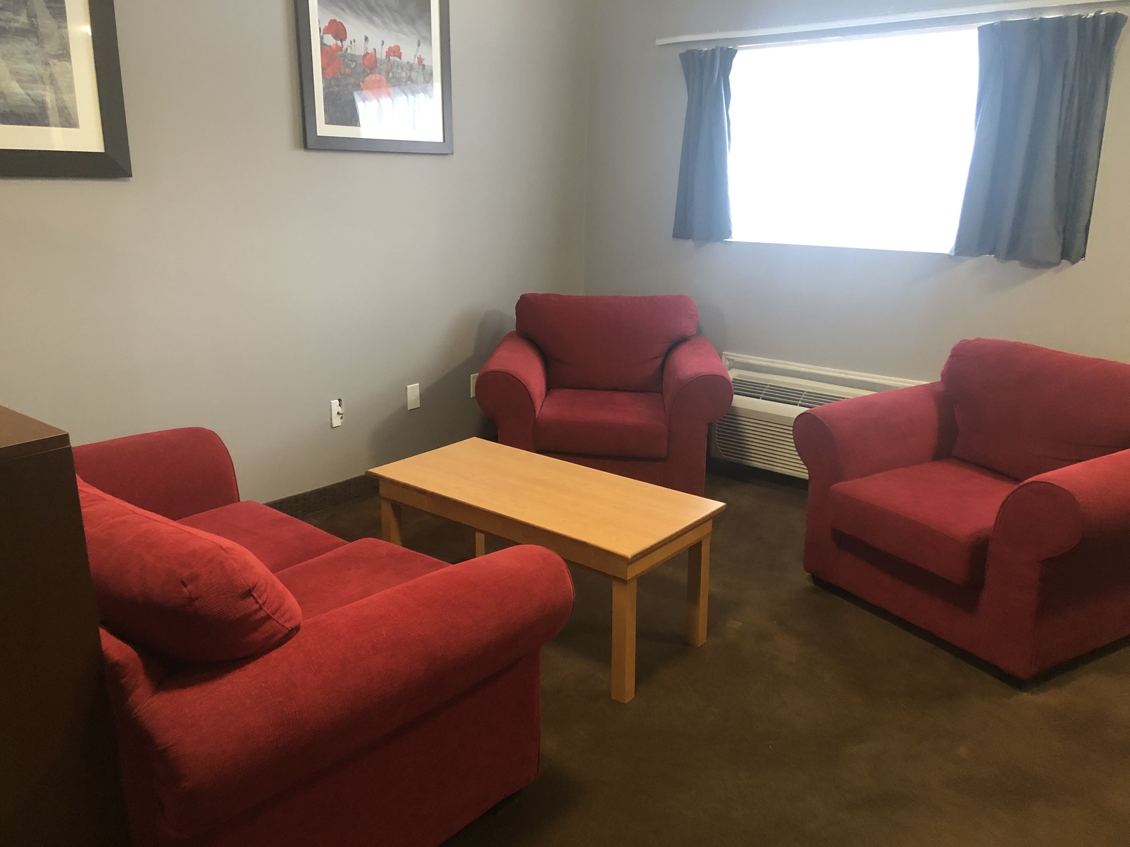 Una habitación con dos sillones rojos, una mesa de centro de madera y un cuadro enmarcado en la pared.