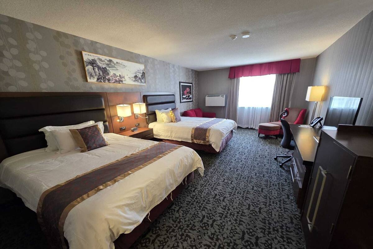 A hotel room with two beds, a desk, a chair, a TV, and a painting on the wall.