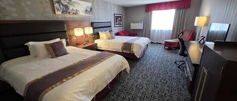 A hotel room with two beds, a desk, a chair, a TV, and a painting on the wall.