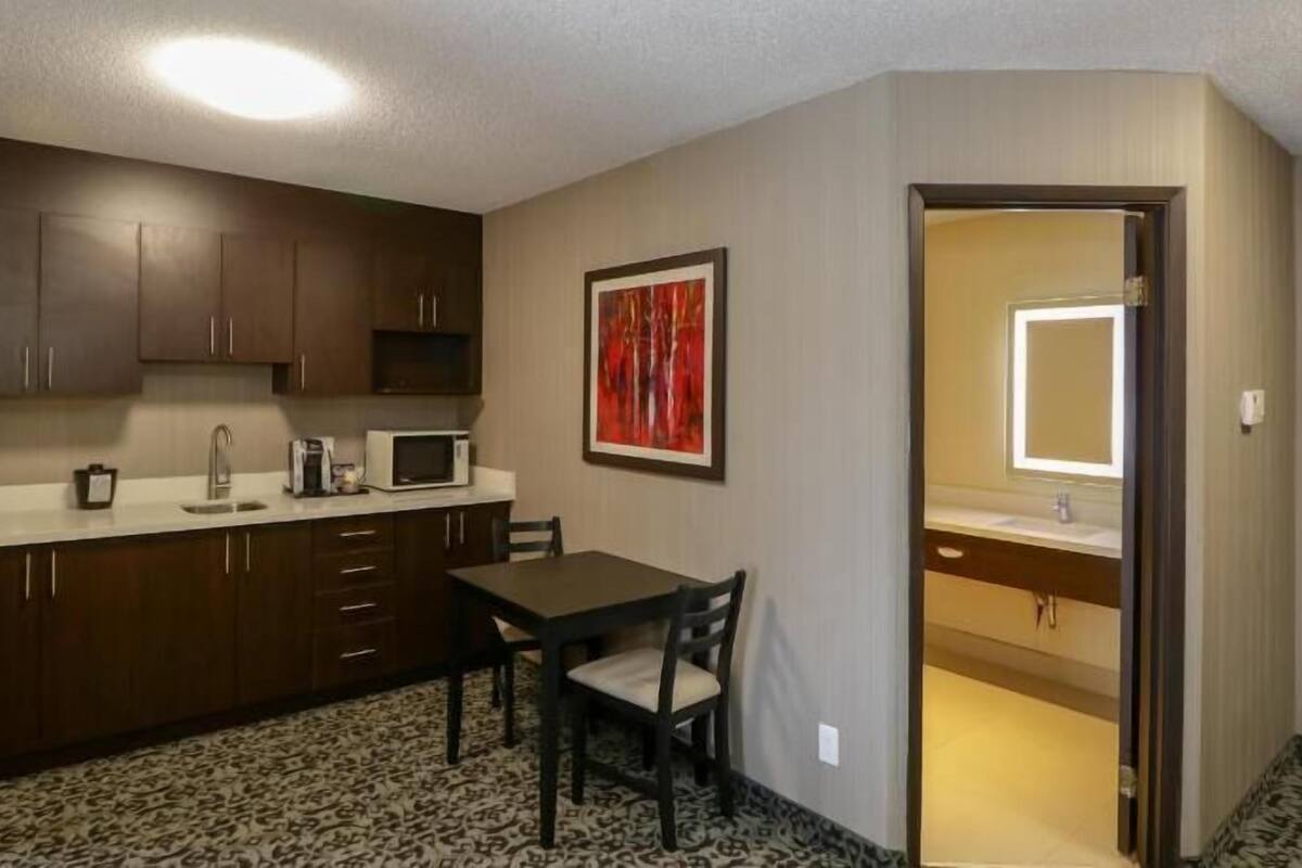 A compact kitchen with dark cabinets, a white countertop, a microwave, and a dining table with two chairs.