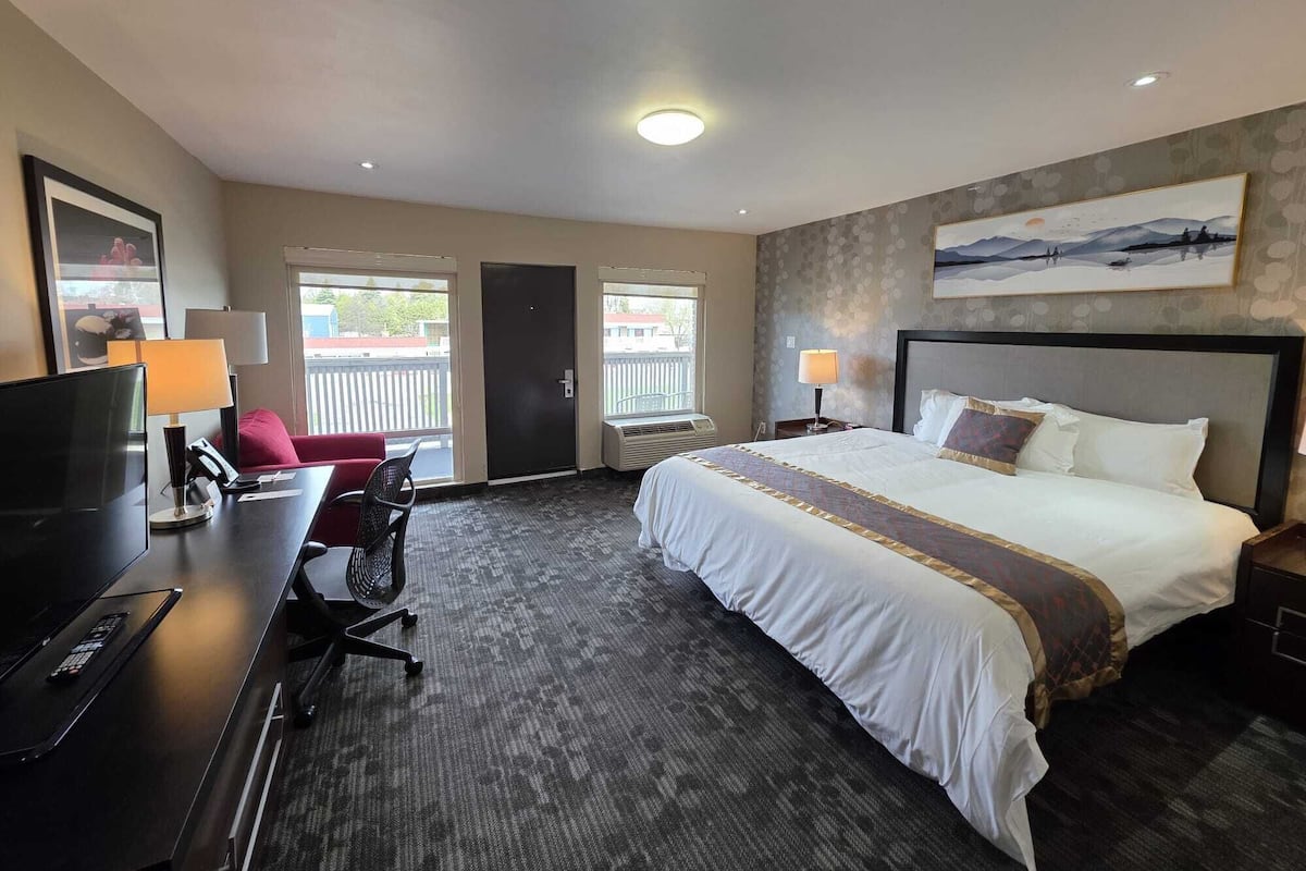 A hotel room with a bed, desk, chair, TV, and windows.
