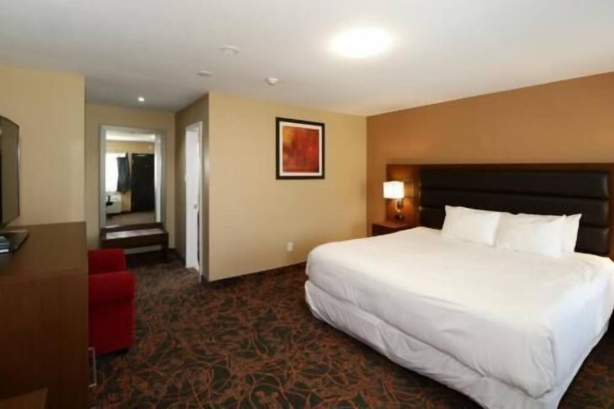 A hotel room with a large bed, a desk, a chair, and a carpeted floor.