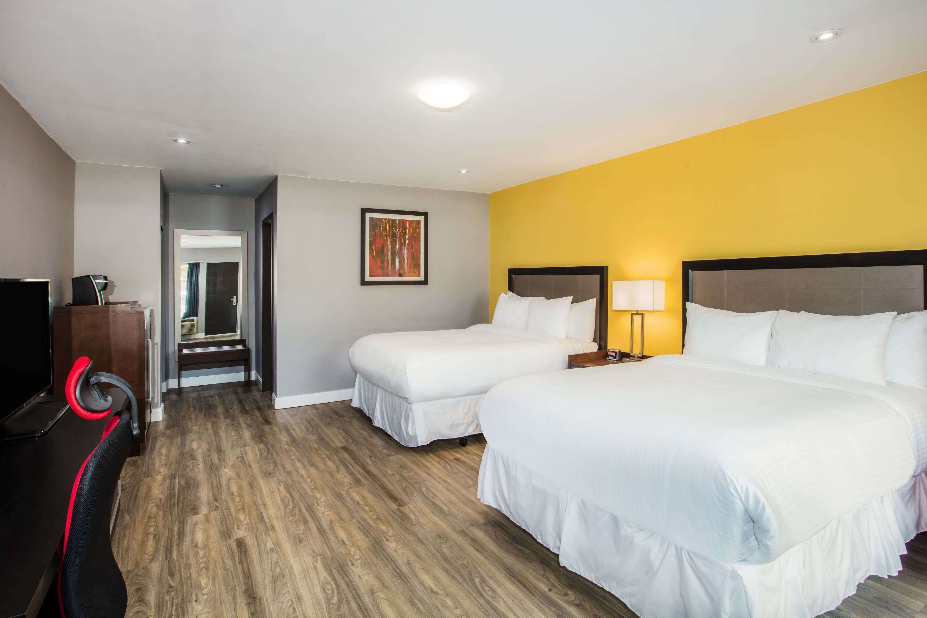 A hotel room with two beds, a TV, a desk with a chair, and a painting on the wall.