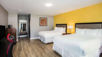 A hotel room with two beds, a TV, a desk with a chair, and a painting on the wall.