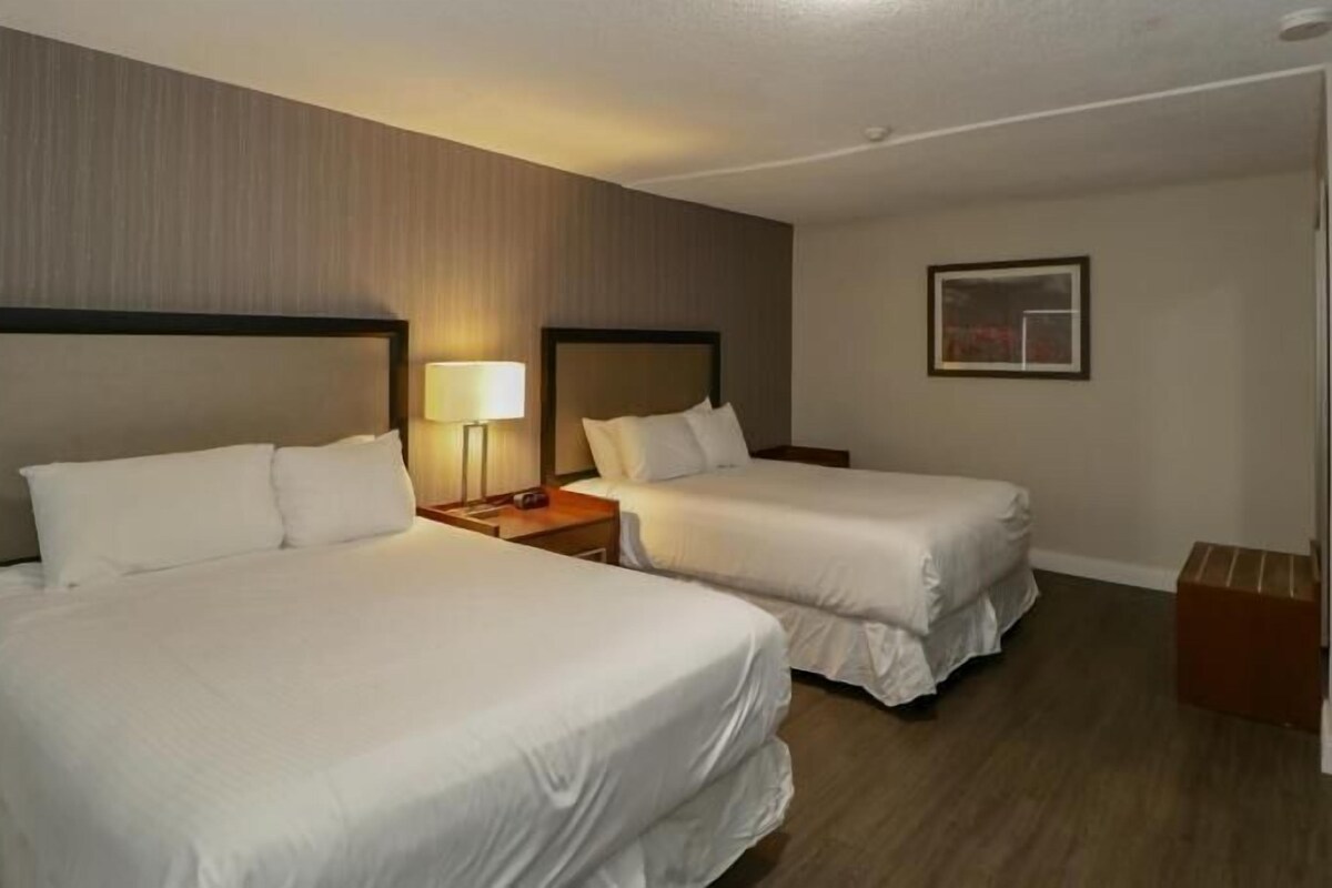 A hotel room with two beds, a nightstand, a lamp, and a framed picture on the wall.