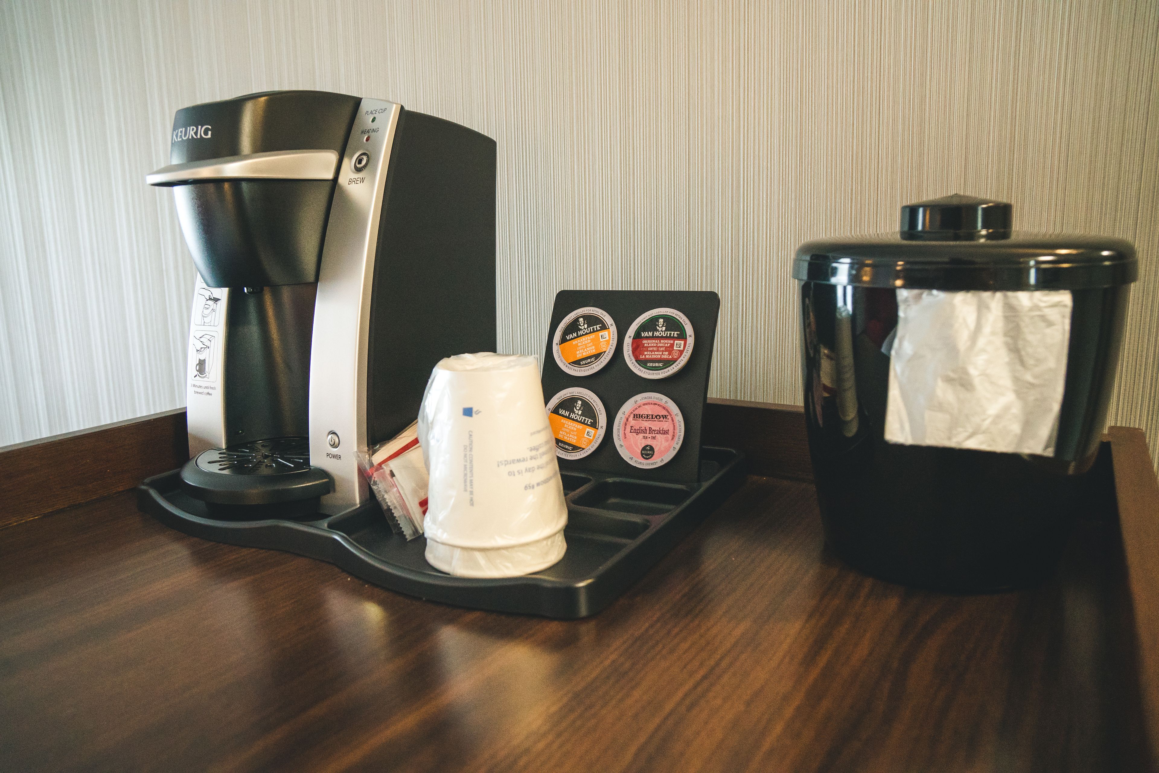 Una cafetera, una taza de café y un cubo de basura sobre una superficie de madera.