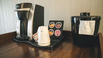 Una cafetera, una taza de café y un cubo de basura sobre una superficie de madera.