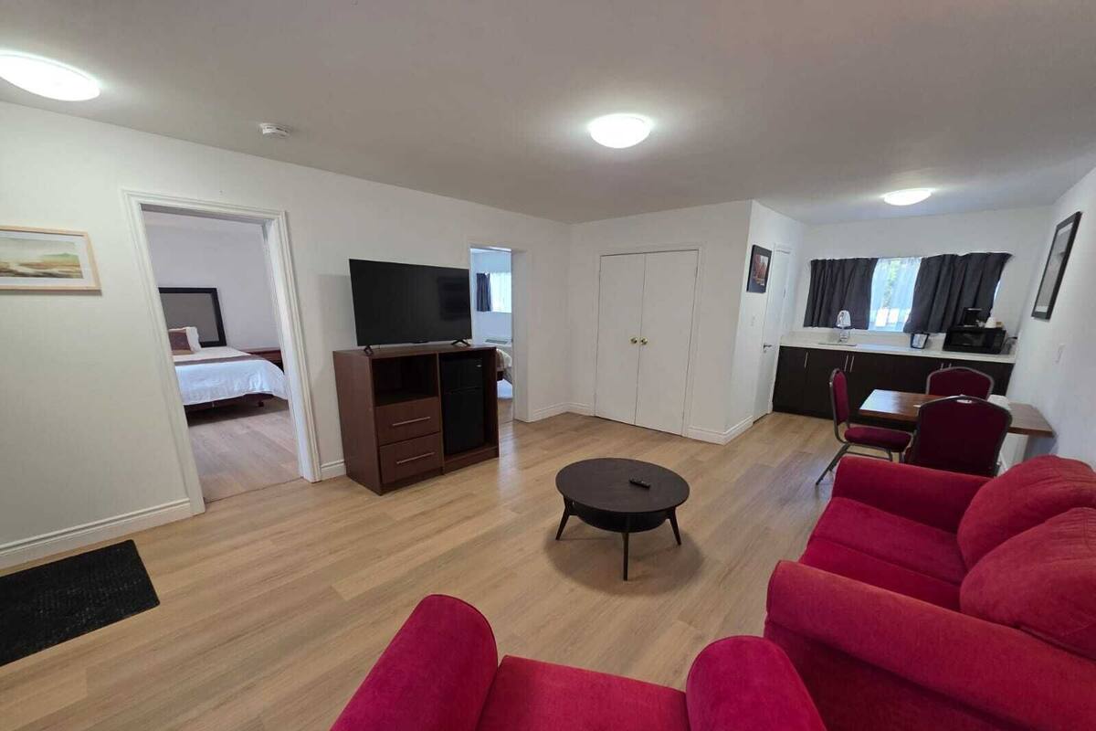 A modern living room with a sofa set, a TV, a small table, and a kitchenette.