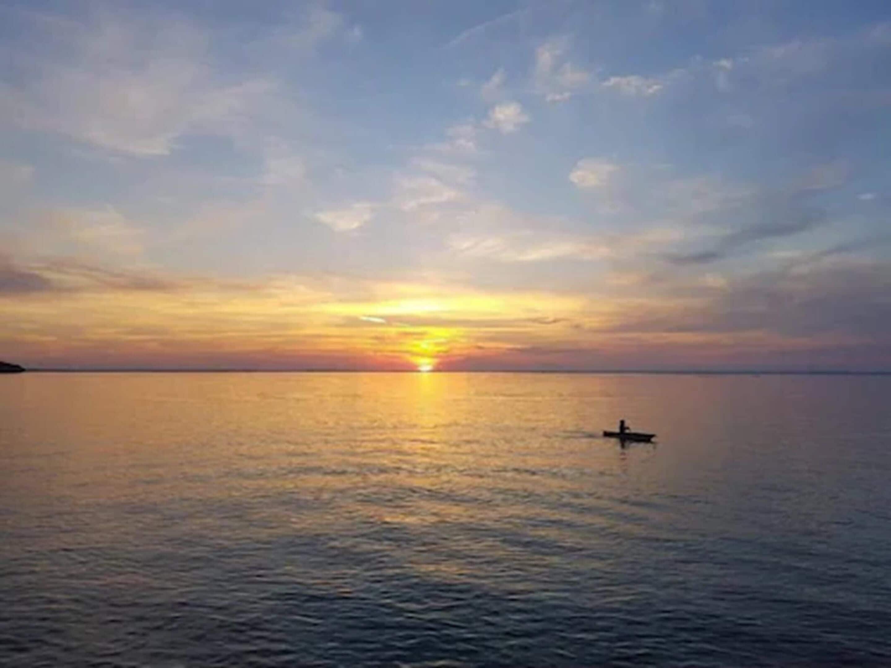 A sunset over a calm sea with a small boat in the distance.