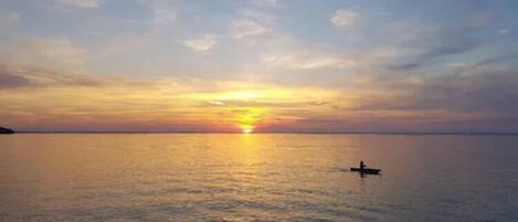 A sunset over a calm sea with a small boat in the distance.