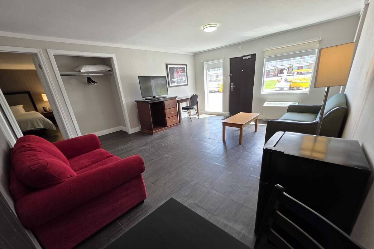 A compact living space with a red sofa, a TV on a wooden cabinet, a dining table, and a chair.